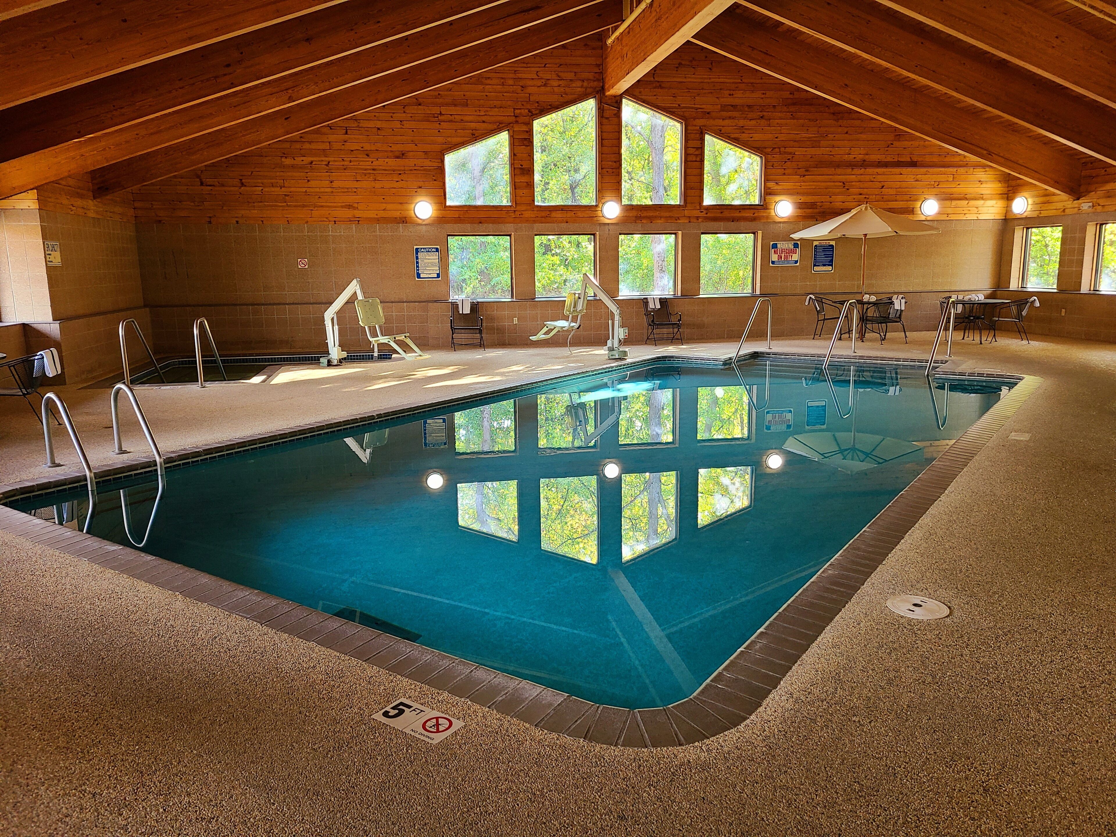 An indoor swimming pool with wooden beams, multiple windows, and a 5 ft depth sign.