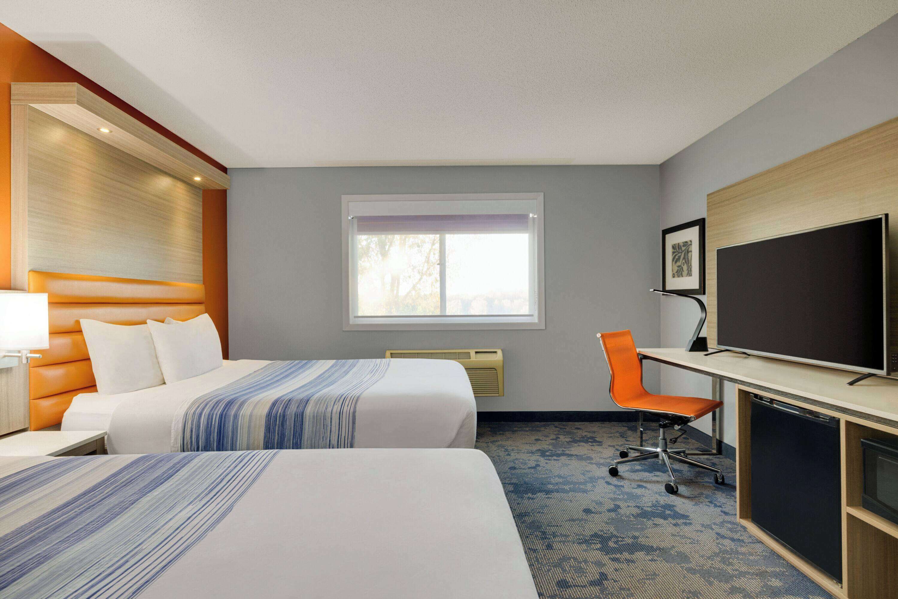 A hotel room with two beds, a desk with a chair, a television, and a window.