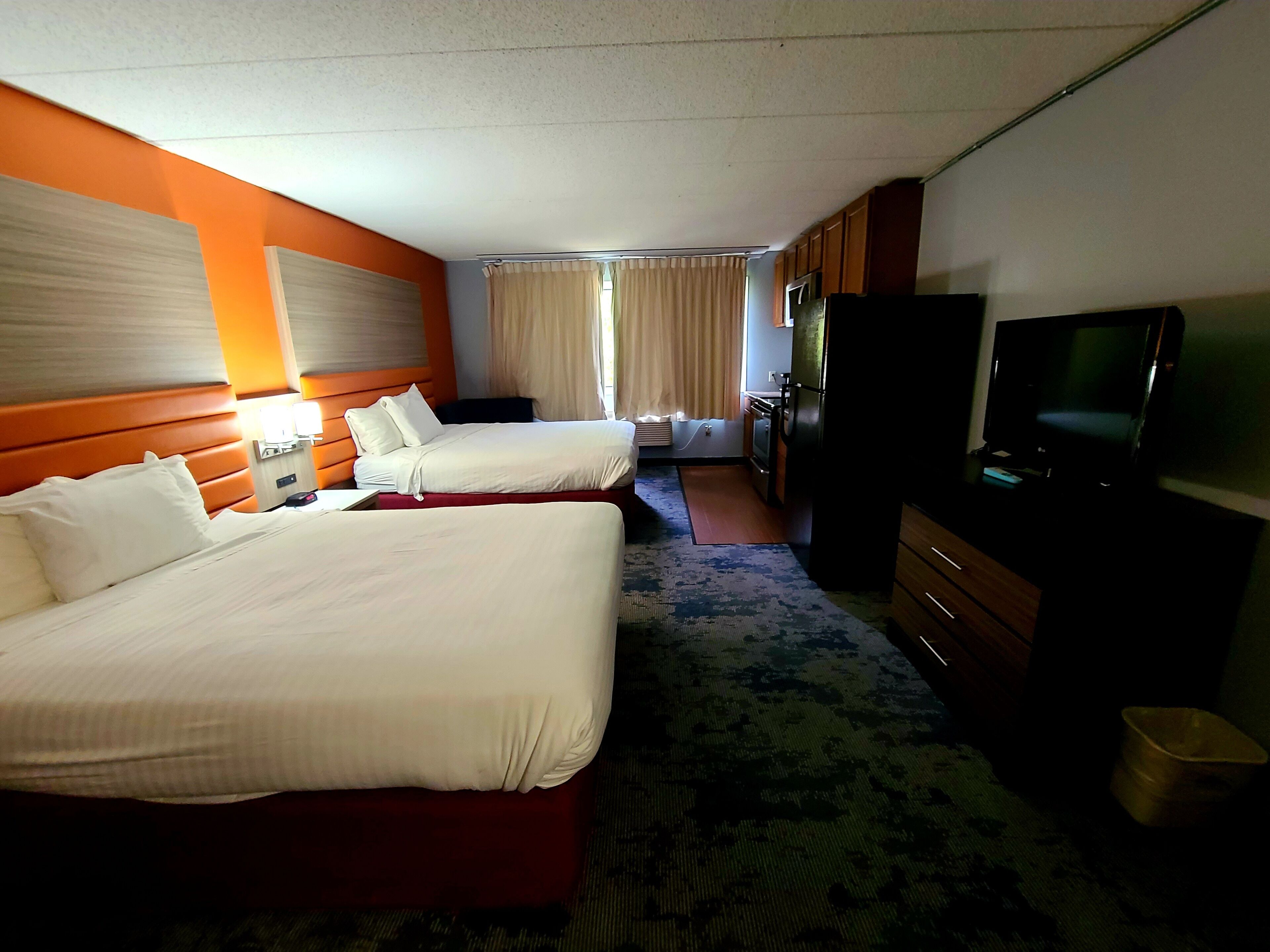Habitación de hotel con dos camas, televisión, escritorio y ventana con cortinas.