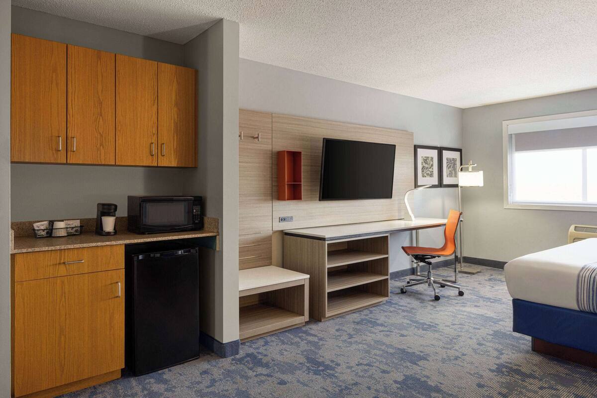 Een compacte hotelkamer met kitchenette, bureau, stoel, bed en televisie.