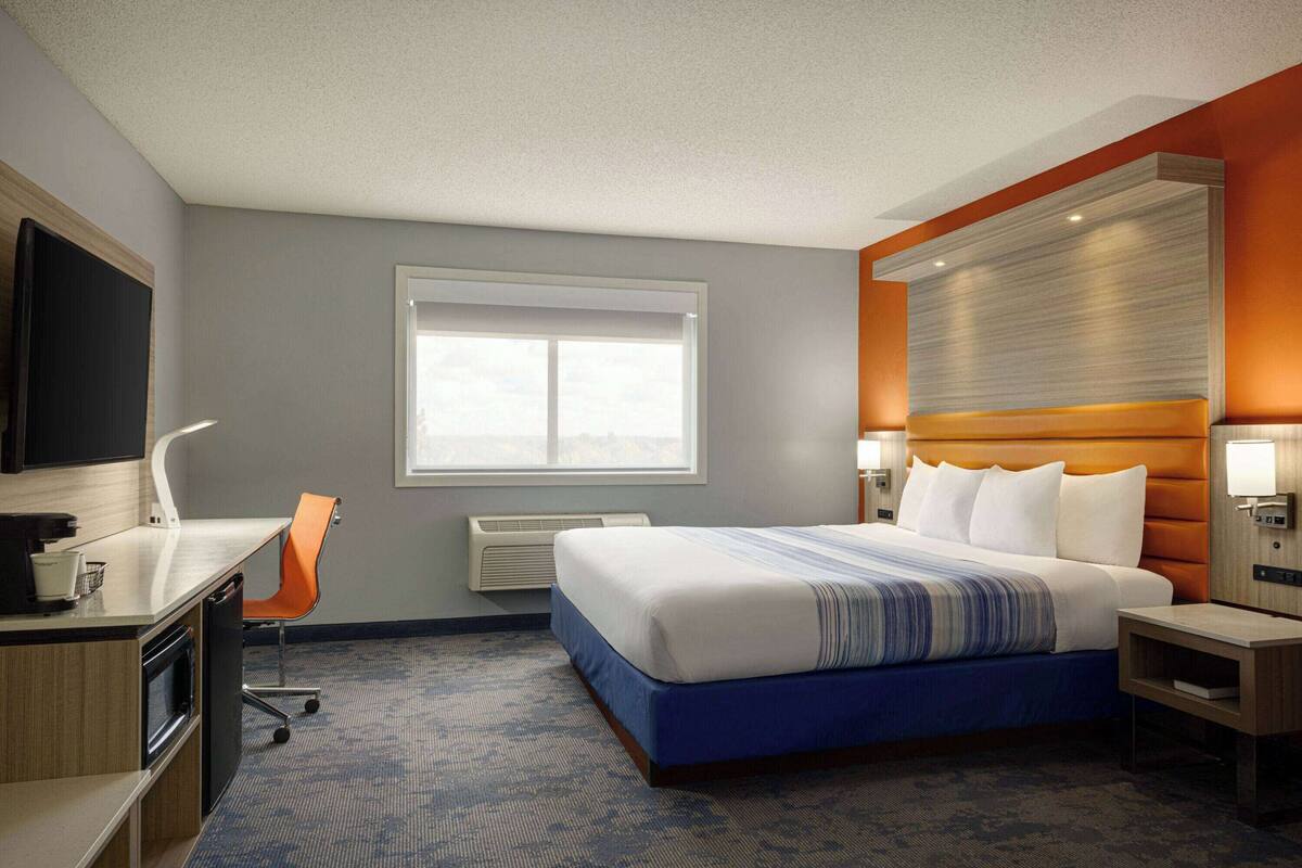 Een hotelkamer met een groot bed, een bureau met stoel, een televisie en een raam.