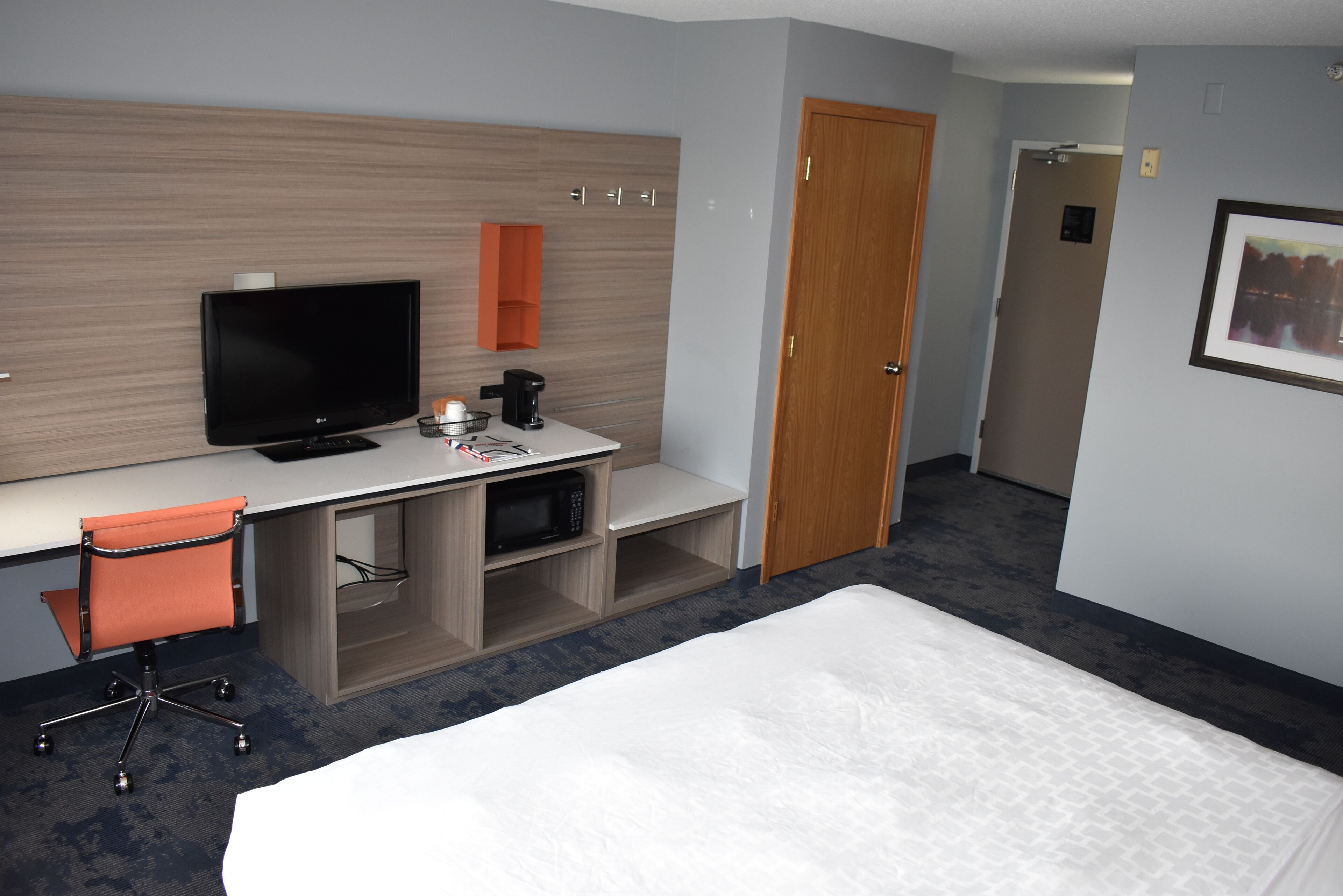 A hotel room with a bed, a desk with a TV, a microwave, and a chair.