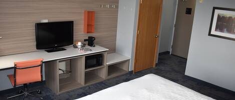 A hotel room with a bed, a desk with a TV, a microwave, and a chair.