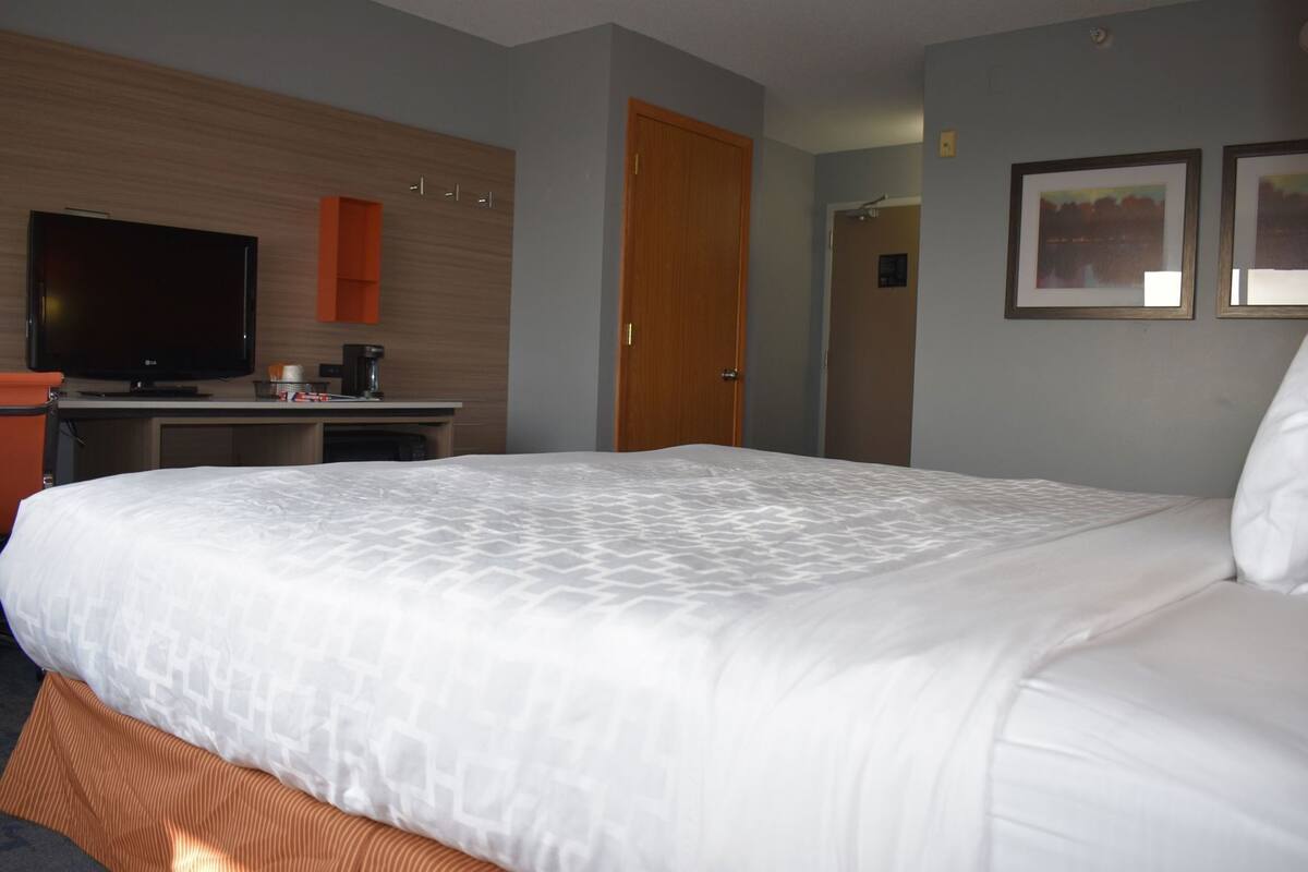 Hotelkamer met een groot bed, een bureau met een flatscreen televisie, een koffieapparaat en twee ingelijste foto's aan de wand.