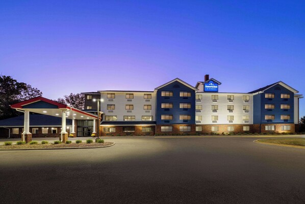 A hotel with a covered parking area, multiple floors, and a sign indicating it is an American Inn Express. - AmericInn by Wyndham Inver Grove Heights Minneapolis (Inver Grove Heights)