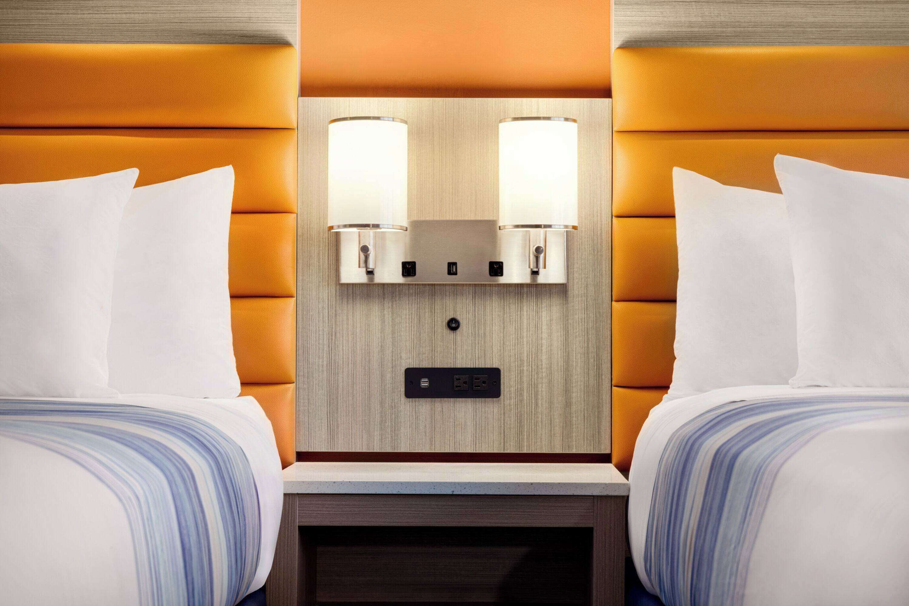Habitación de hotel con dos camas, cabecero de madera y mesita de noche con reloj digital.