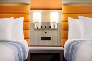 Habitación de hotel con dos camas, cabecero de madera y mesita de noche con reloj digital.