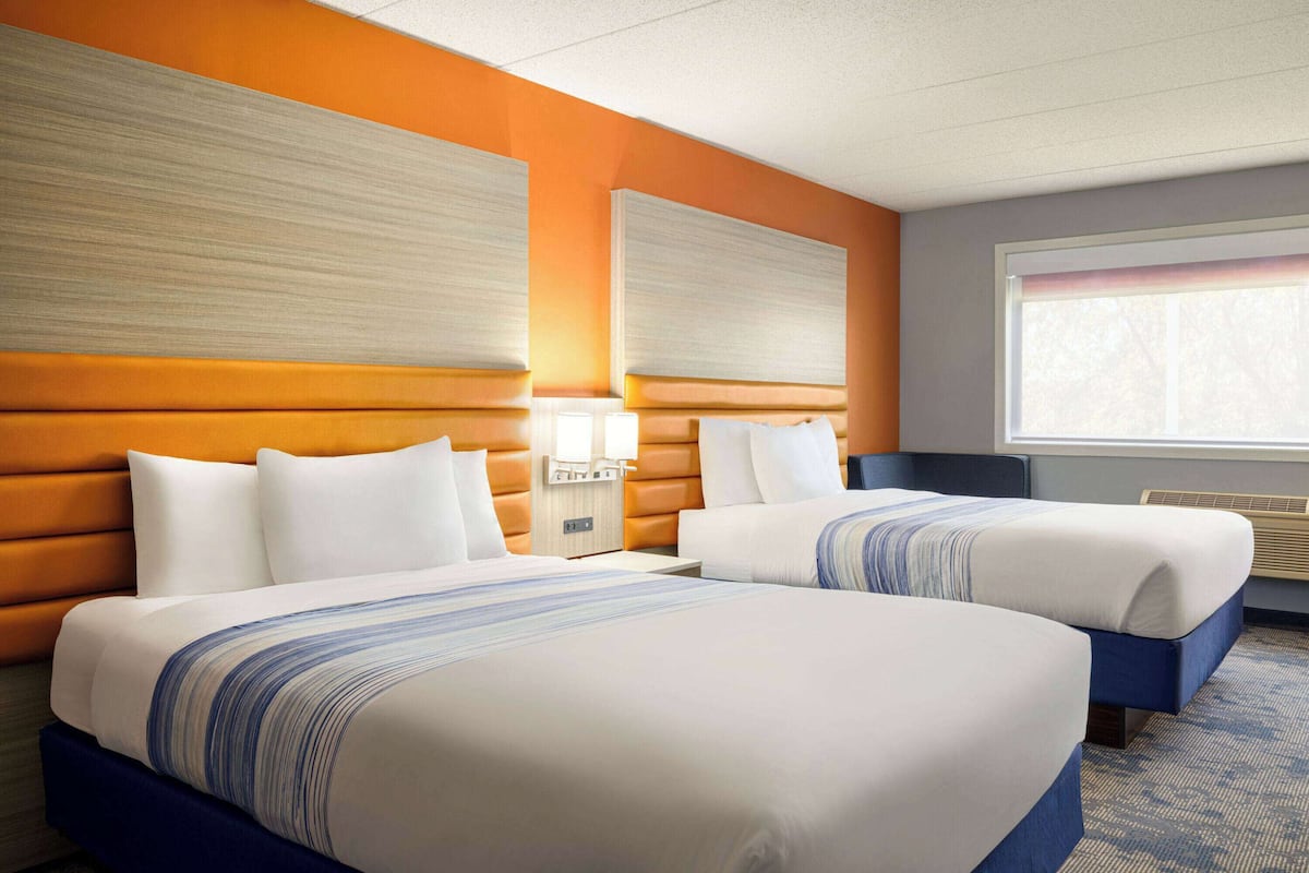 Een hotelkamer met twee bedden, een groot raam en een wandlamp.