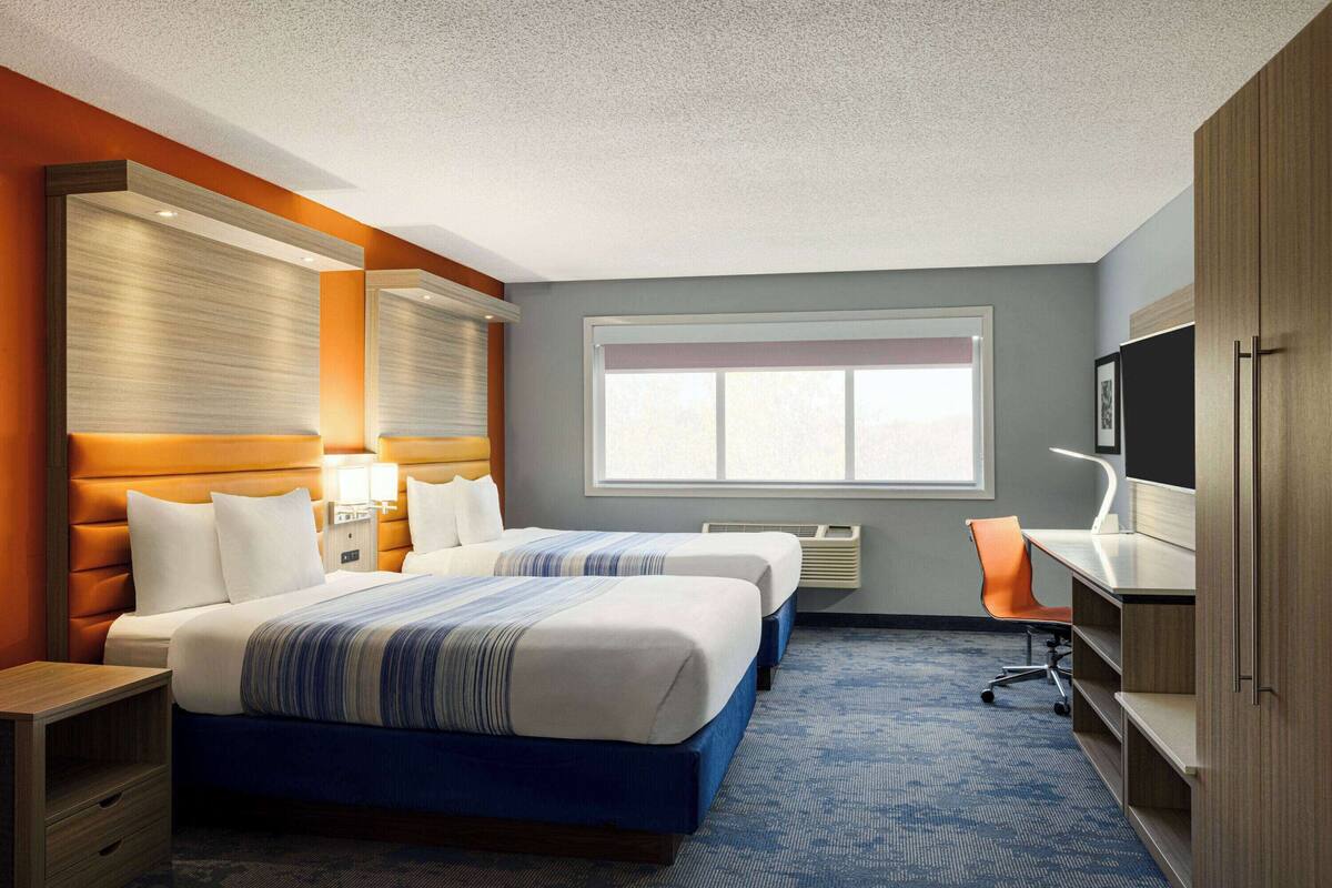 Een hotelkamer met twee bedden, een bureau, een stoel, een televisie en een raam.