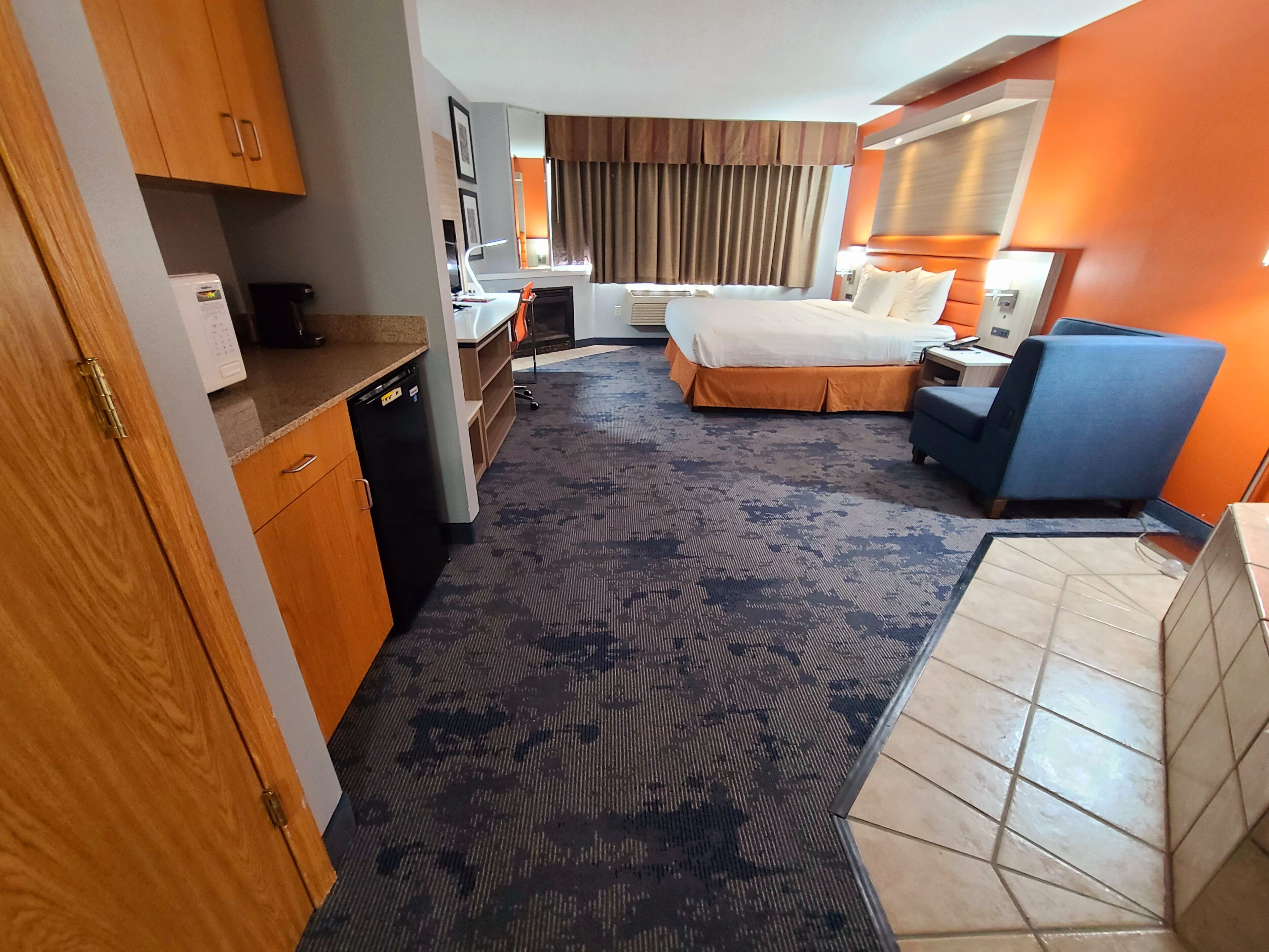 Habitación de hotel con cama, escritorio, silla y una pequeña cocina.