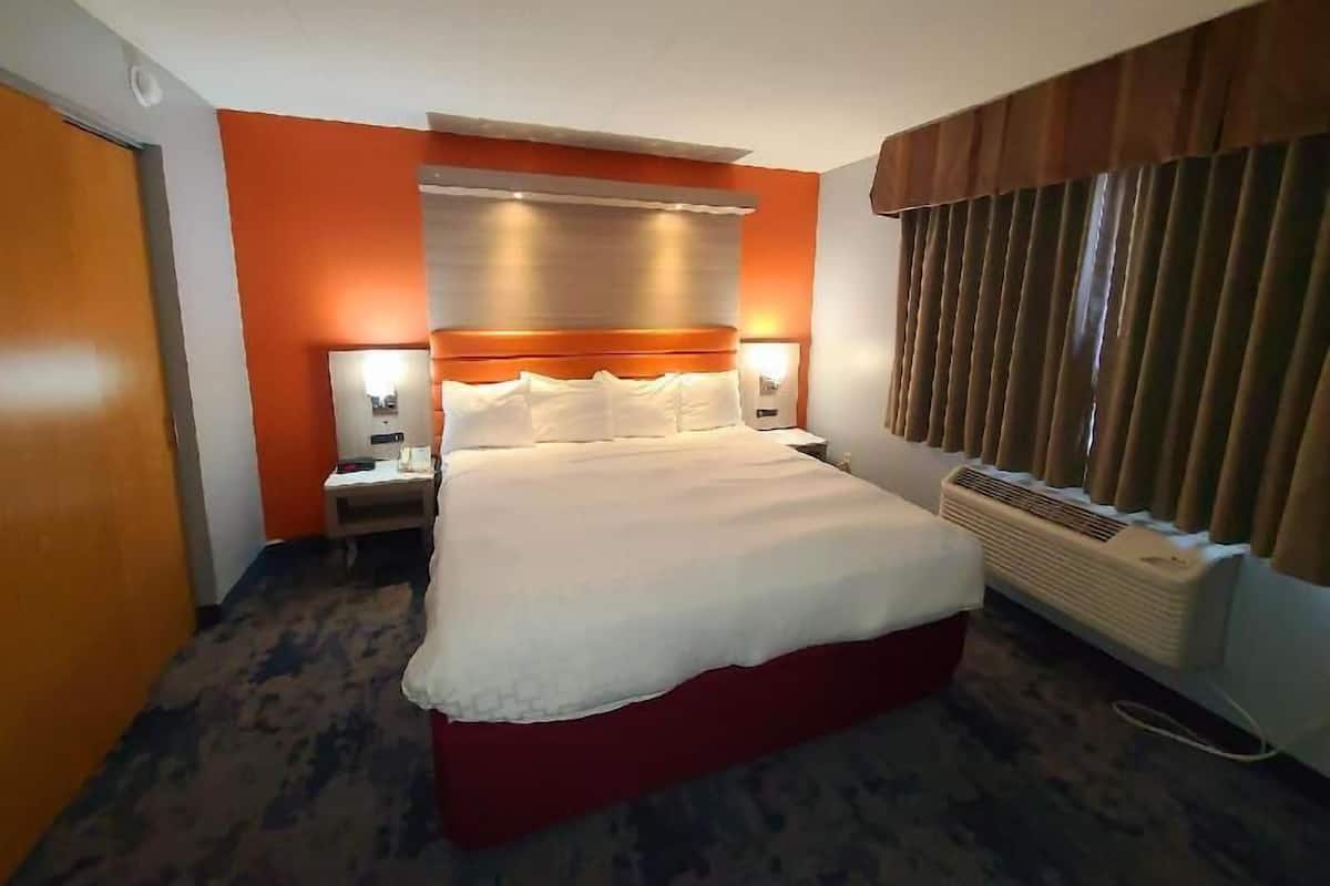 Een hotelkamer met een groot bed, een nachtkastje, een lamp, een verwarming en een raam met gordijnen.