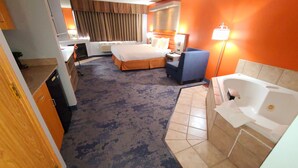 Habitación de hotel con cama, escritorio, silla, baño con bañera y piso alfombrado.