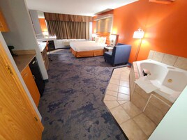 A hotel room with a bed, a desk, a chair, a bathroom with a bathtub, and a carpeted floor.