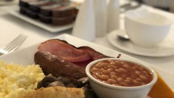 A breakfast plate with eggs, bacon, mushrooms, toast, beans, and a slice of orange.