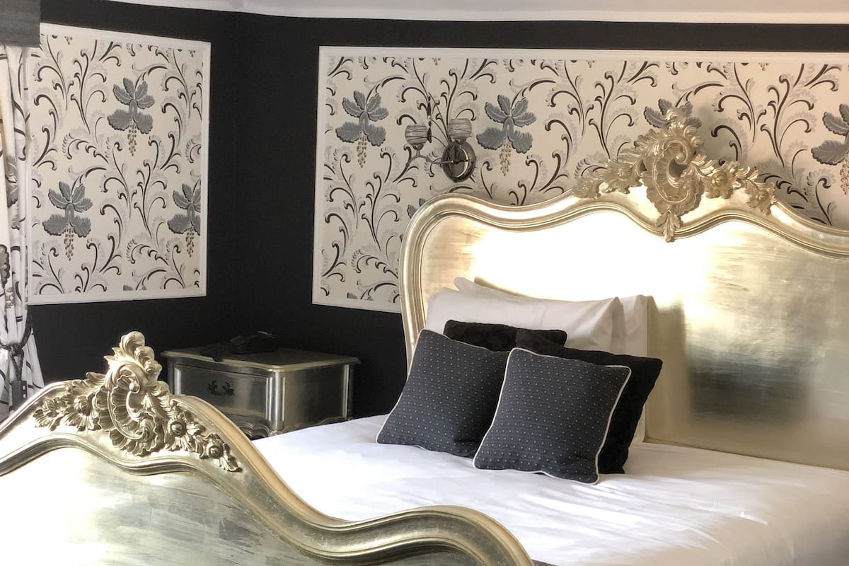A bed with an ornate headboard, a black upholstered bench, and a patterned wallpaper on the walls.