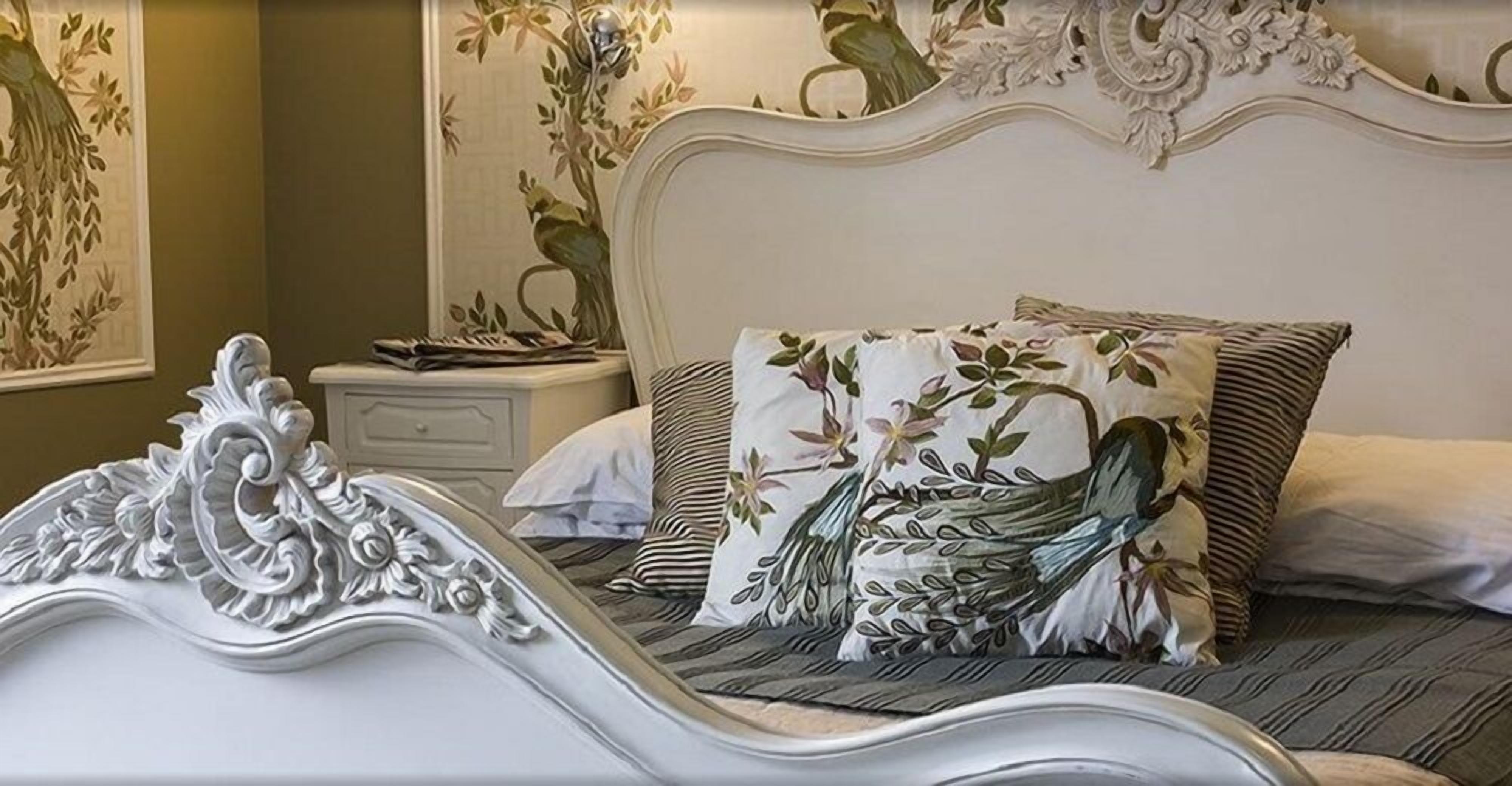 A bed with ornate headboard, floral-patterned pillows, and a striped bedspread.