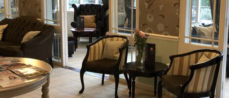 A cozy room with a sofa, two armchairs, a small table with magazines, and a vase with flowers.
