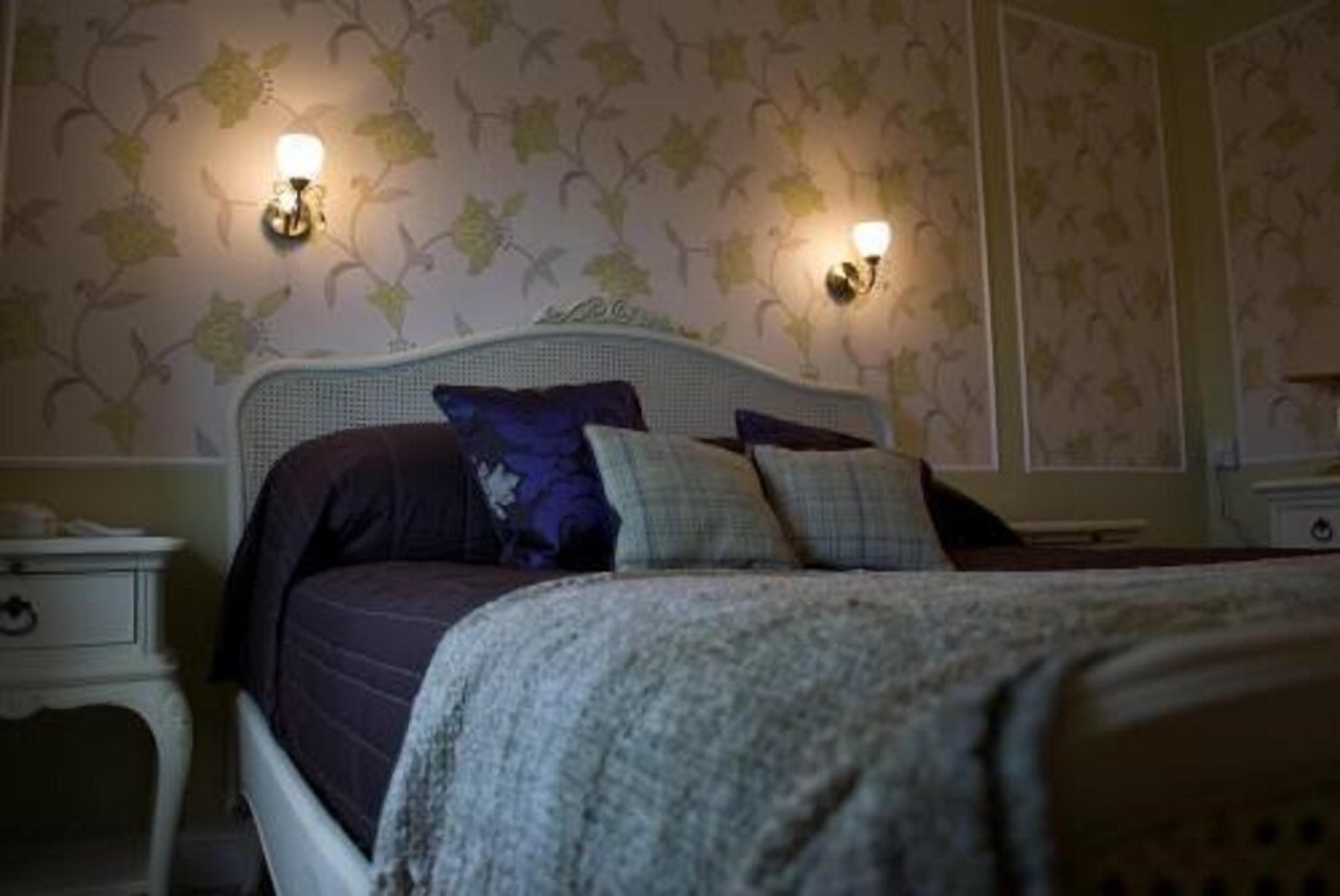 Quarto com uma cama, duas luminárias na parede e uma mesa de cabeceira.