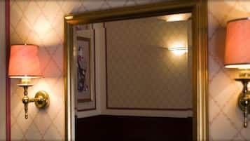 A hotel room with a patterned wallpaper, a framed artwork on the wall, and two wall-mounted lamps.