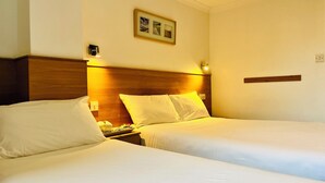 A hotel room with two beds, a wooden headboard, a nightstand with a phone, and a framed picture on the wall. - West Cromwell Hotel (London)