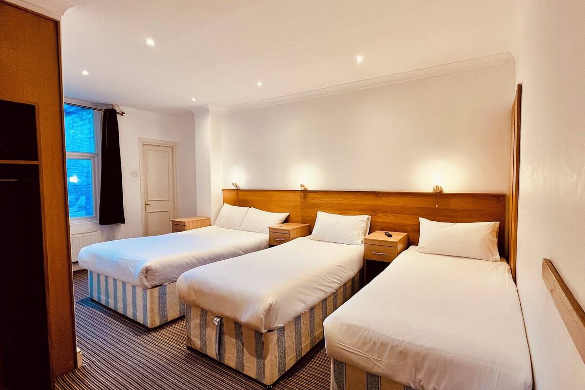 A hotel room with two single beds, a wooden headboard, bedside tables, and a window with curtains.