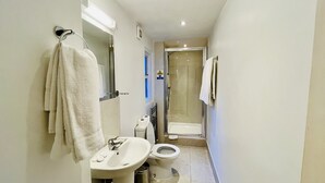 A narrow bathroom with a sink, toilet, and glass shower enclosure. - West Cromwell Hotel (London)