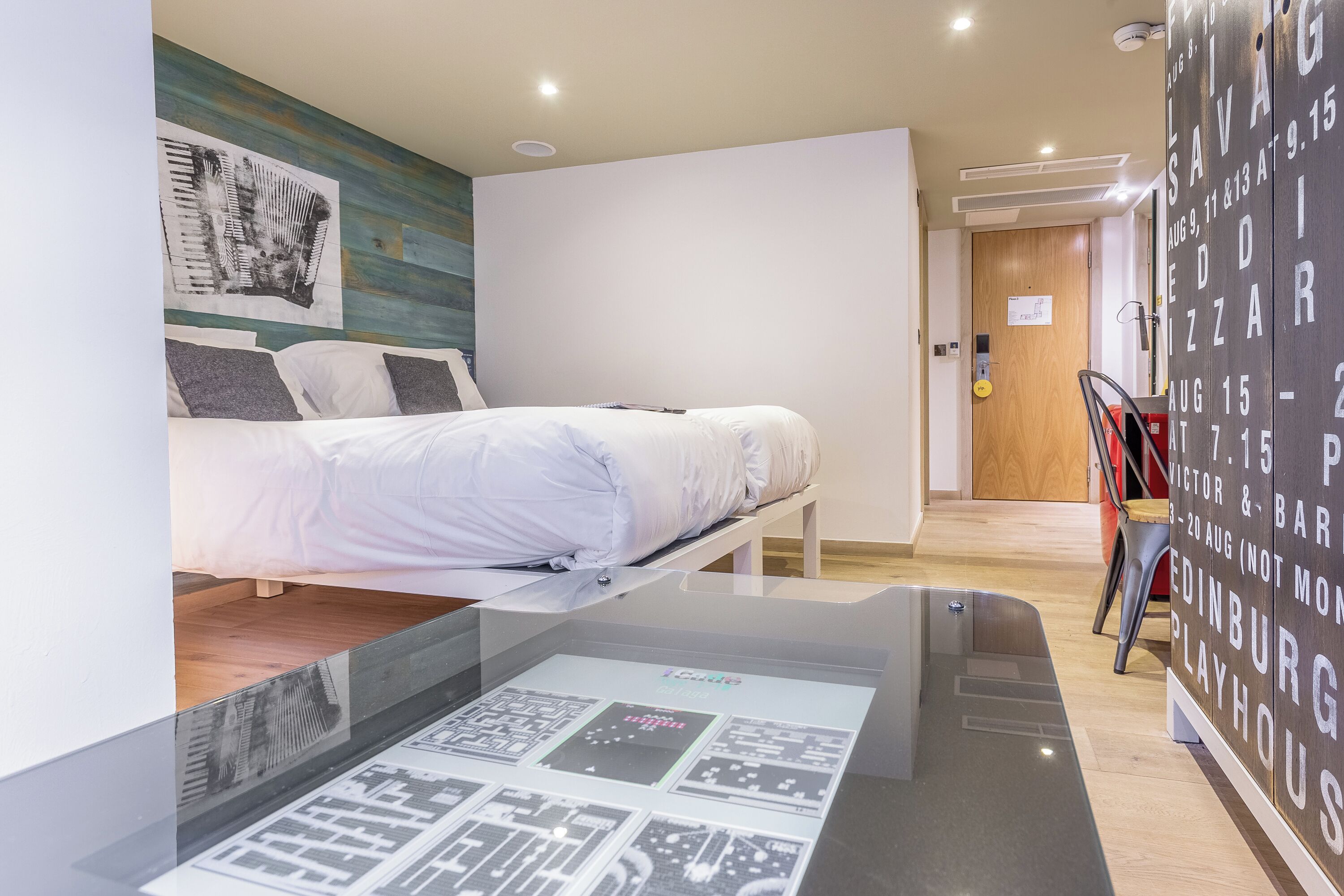 A modern hotel room with a bed, a wall-mounted artwork, and a digital display table.