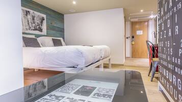 A modern hotel room with a bed, a wall-mounted artwork, and a digital display table.