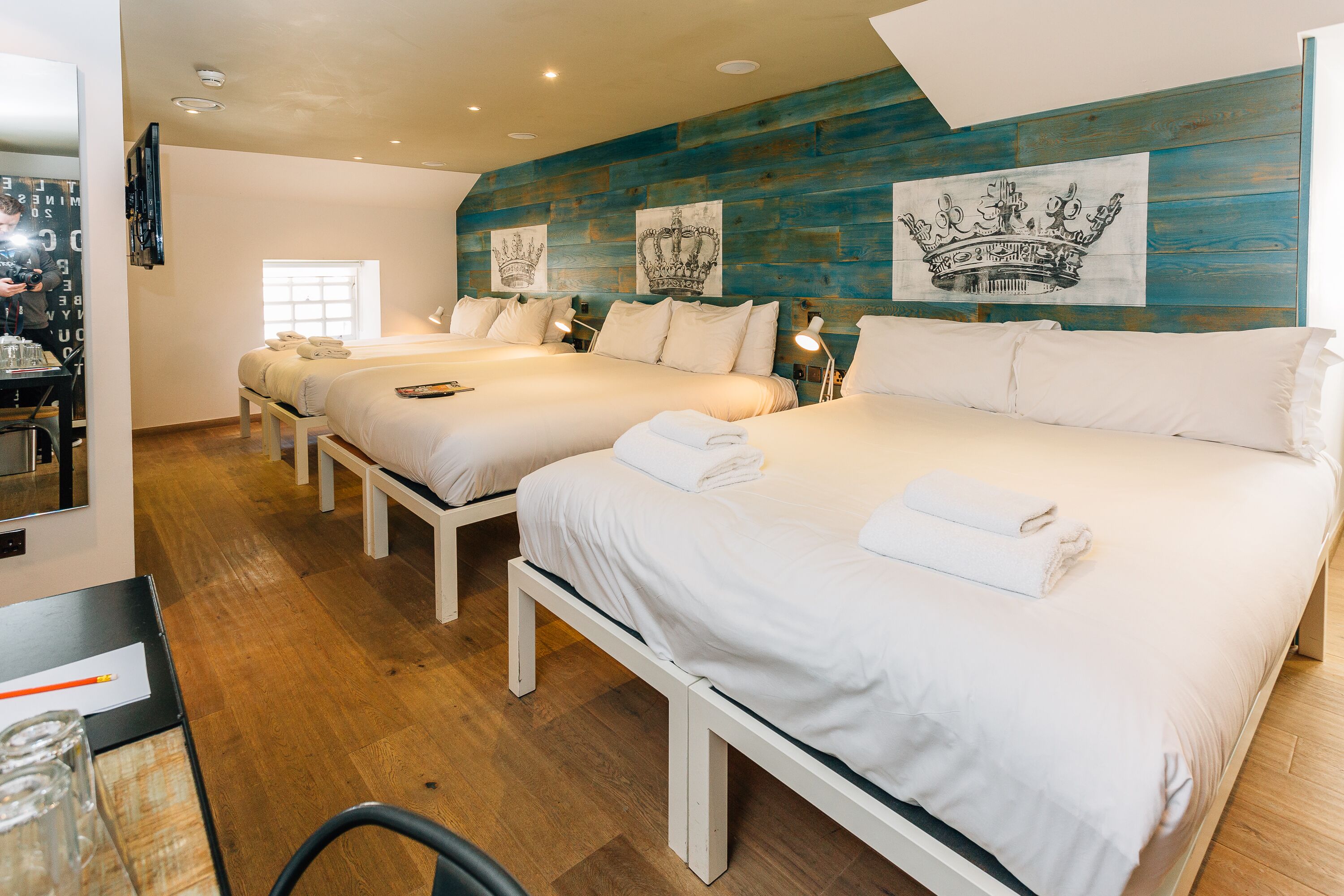 A hotel room with two beds, wooden flooring, and artwork on the wall.