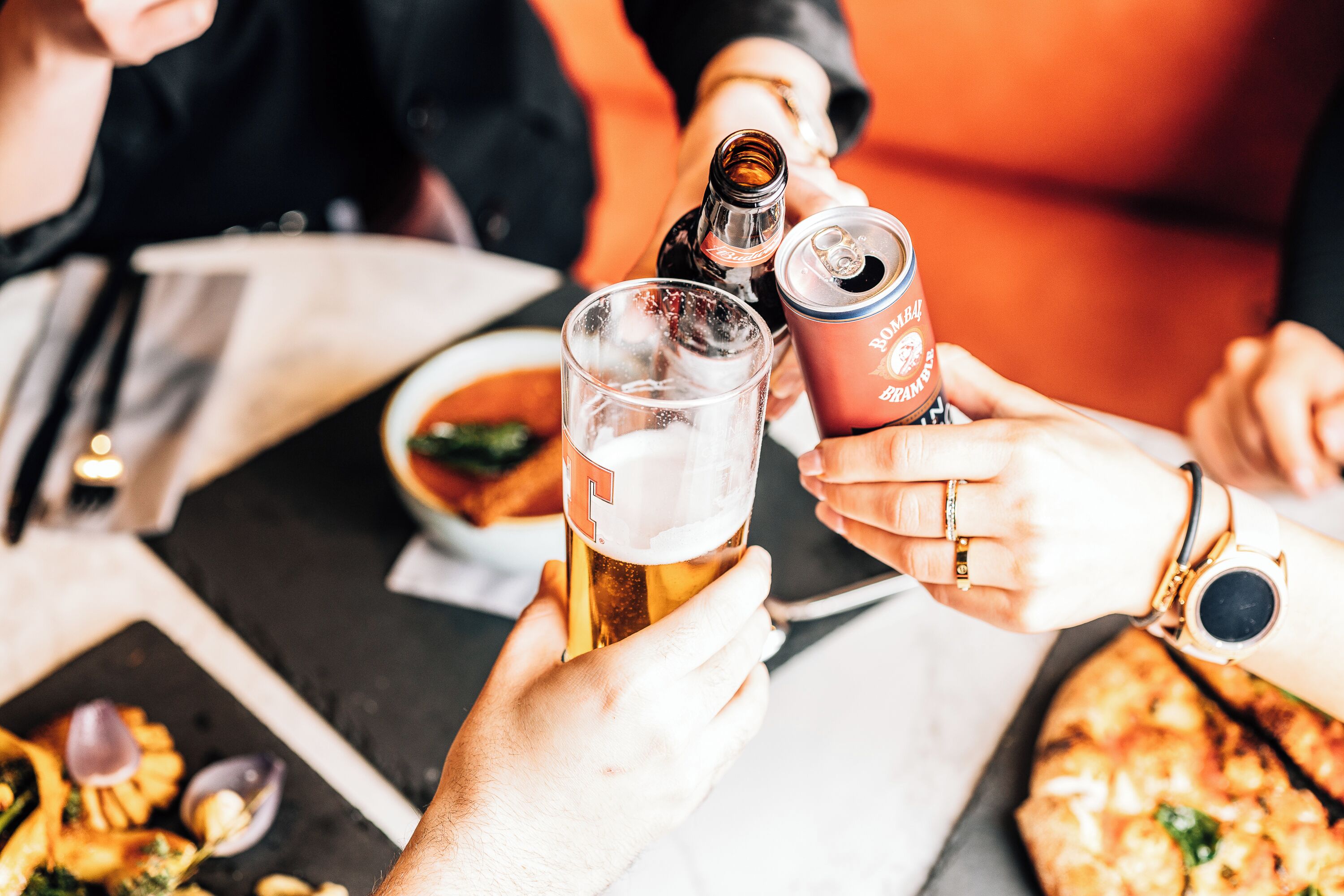 A group of people toasting with beer glasses and a can, with a pizza on the table.