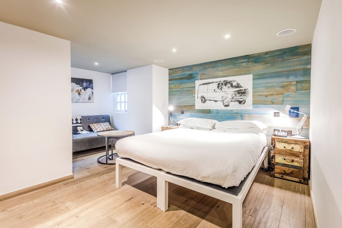Un dormitorio moderno con cama, sofá, suelo de madera y obras de arte en las paredes.