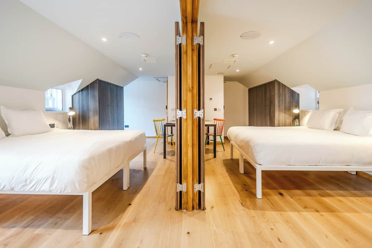 Habitación de hotel moderna con dos camas, un pilar de madera y vistas a la ciudad.