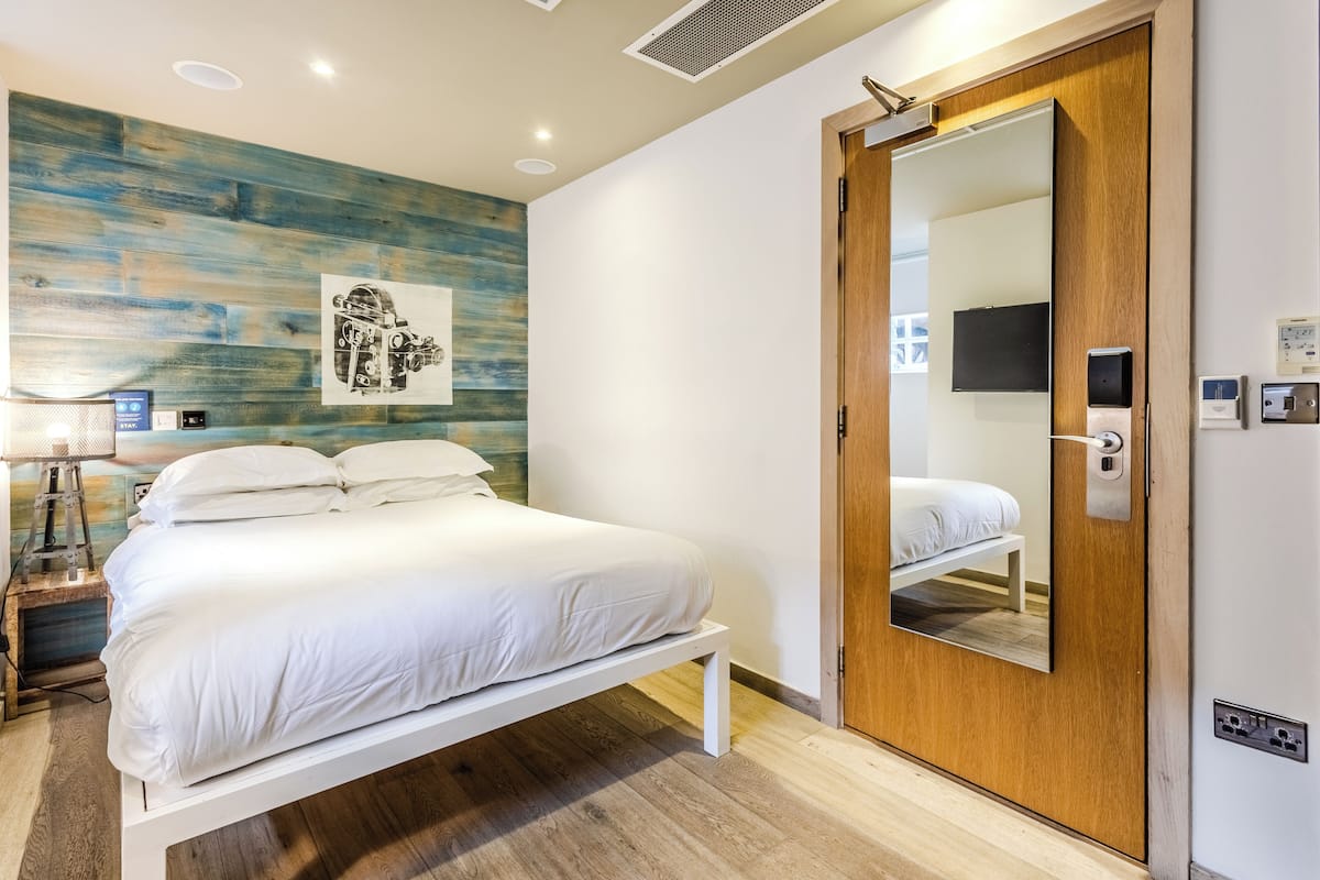 Una habitación de hotel moderna con una cama, una puerta de madera, un espejo y una obra de arte colgada en la pared.