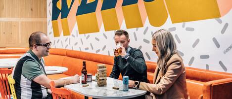 A group of people seated at a table in a brightly lit indoor setting with orange seating and a large wall with stylized text.