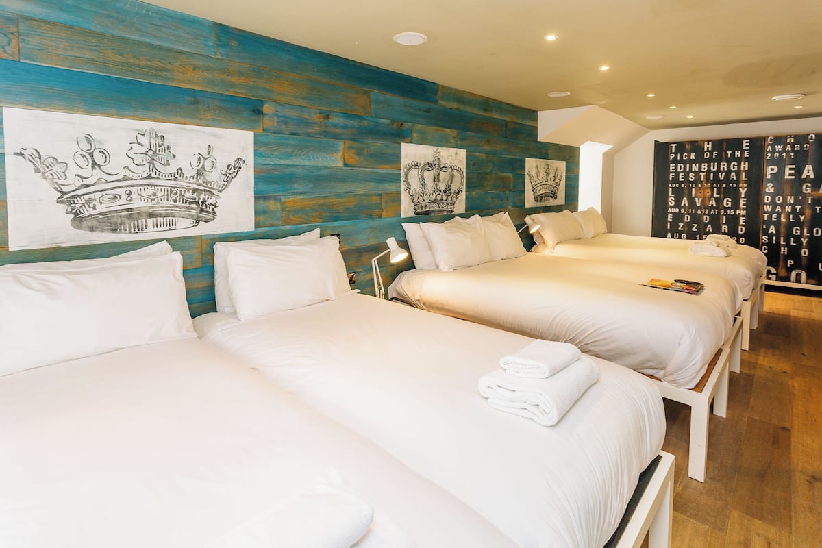Habitación de hotel con tres camas, cada una con ropa blanca y almohadas. Las paredes están decoradas con cuadros, incluyendo un diseño de corona.