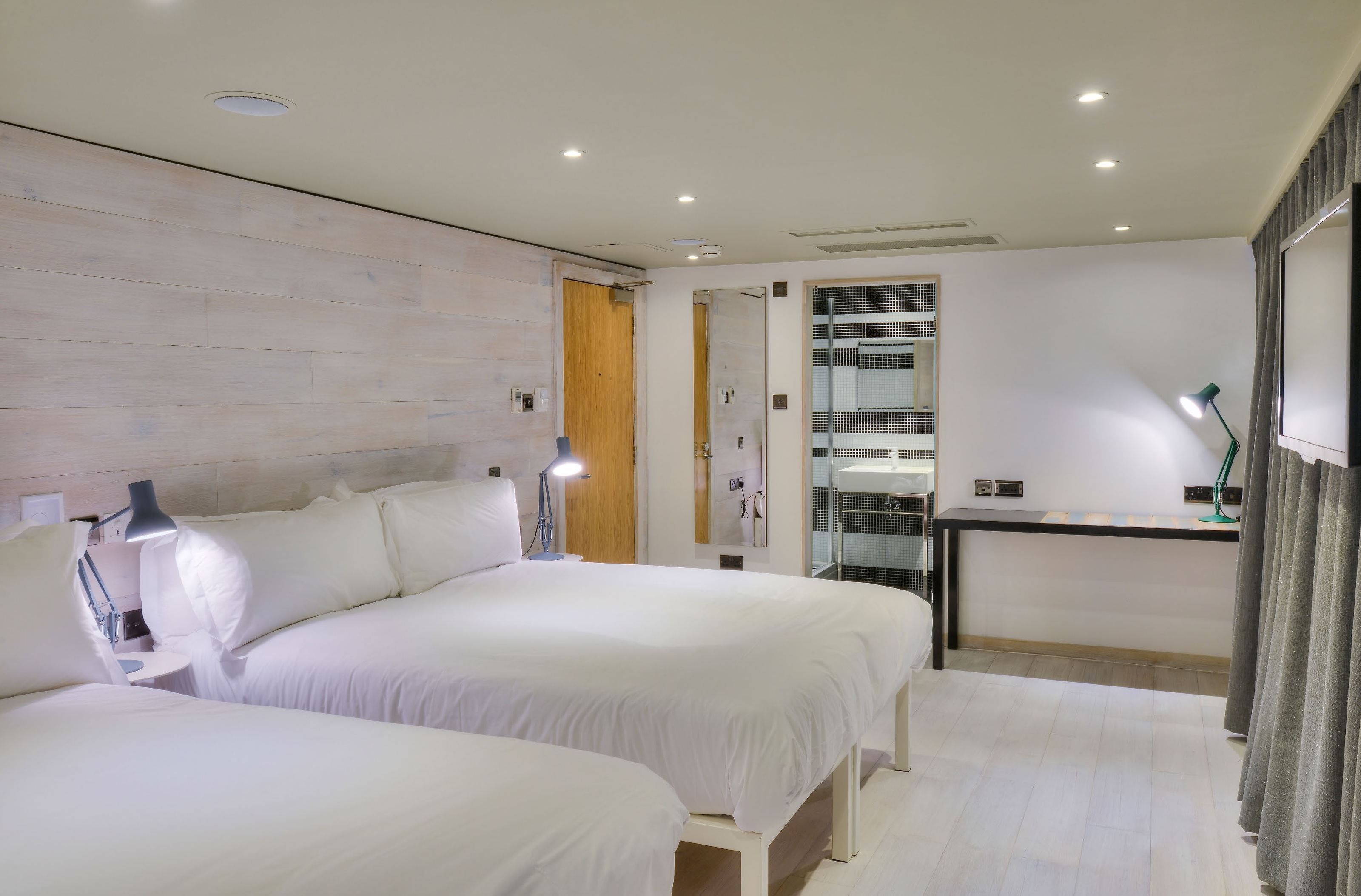 A modern hotel room with two beds, a small desk, and a mirror.