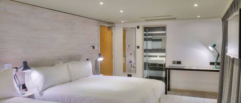 A modern hotel room with two beds, a small desk, and a mirror.