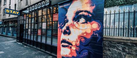 A building with a large mural on the side, a sign that says "STAY", and a window display advertising cakes.