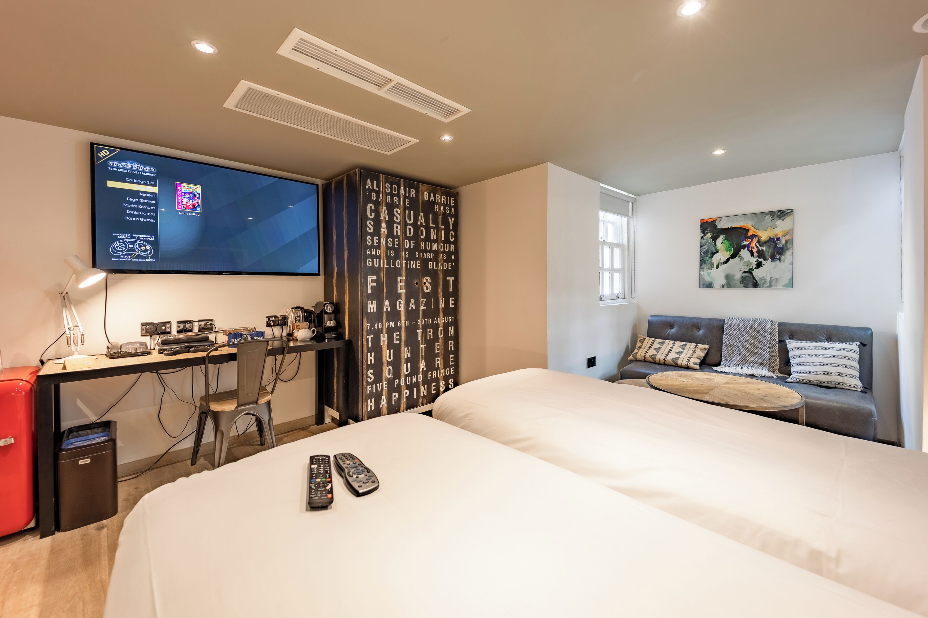 Una habitación de hotel moderna con una cama grande, un escritorio con computadora, un televisor y una obra de arte colgada en la pared.
