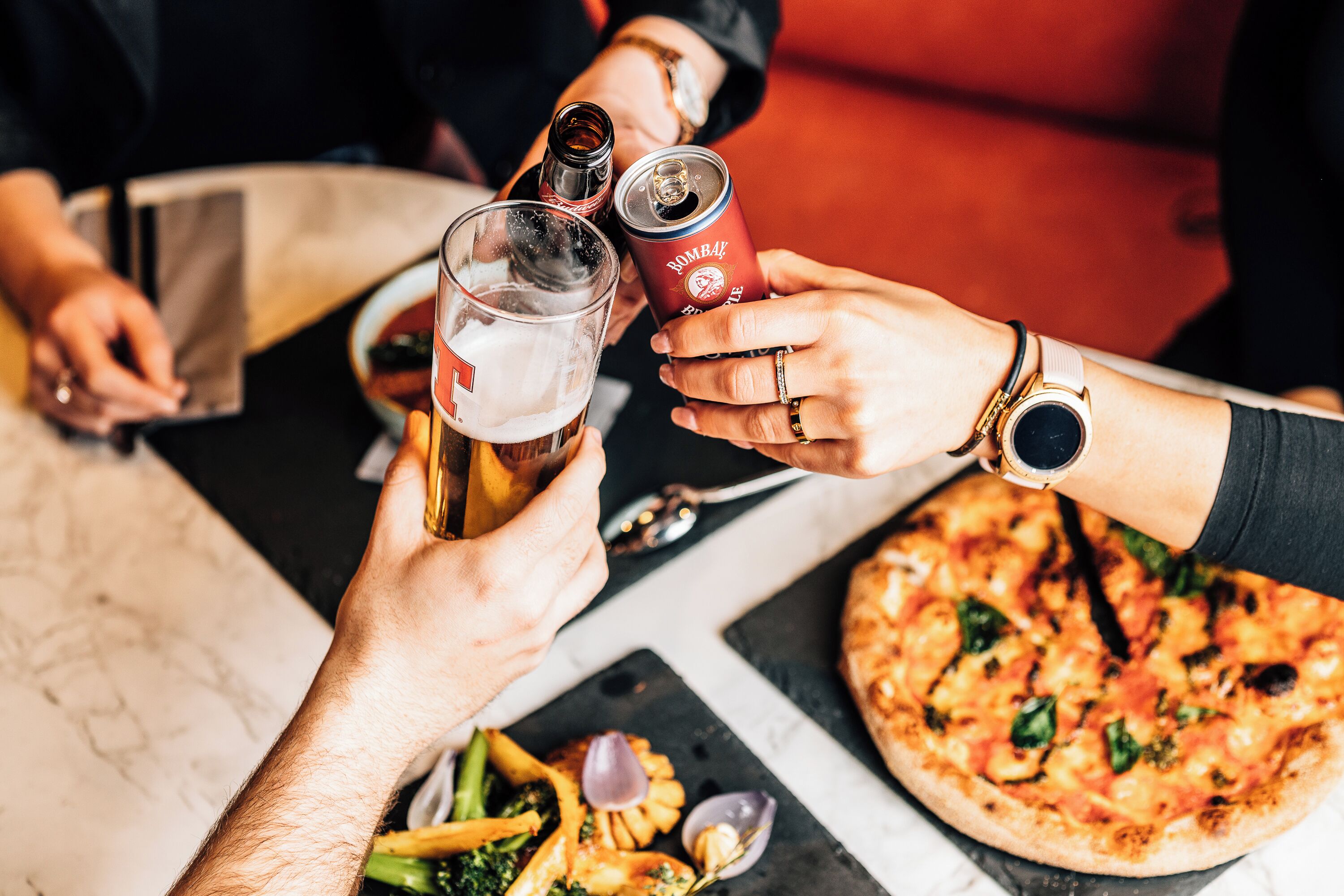 Un groupe de personnes trinquant avec des boissons et partageant une pizza autour d’une table.