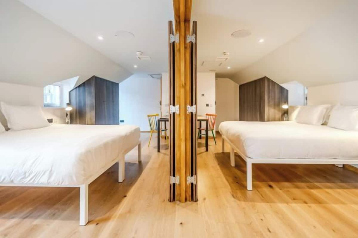 Habitación de hotel moderna con dos camas, un pilar de madera y vista a la ciudad.