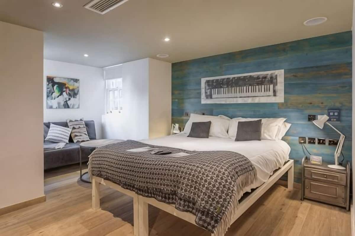 Un dormitorio moderno con cama, mesita de noche y una pared decorada con un cuadro grande.
