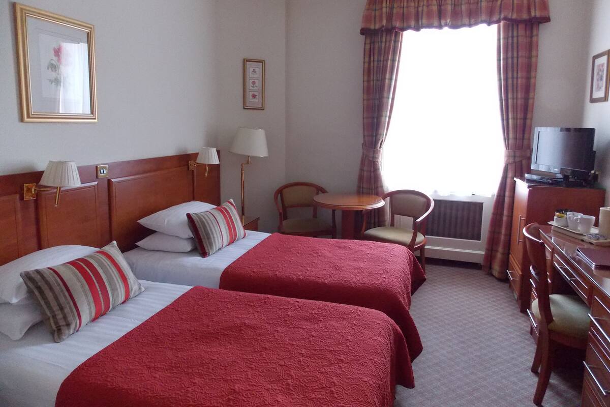 A hotel room with two beds, a desk, a chair, a television, and a window with curtains.