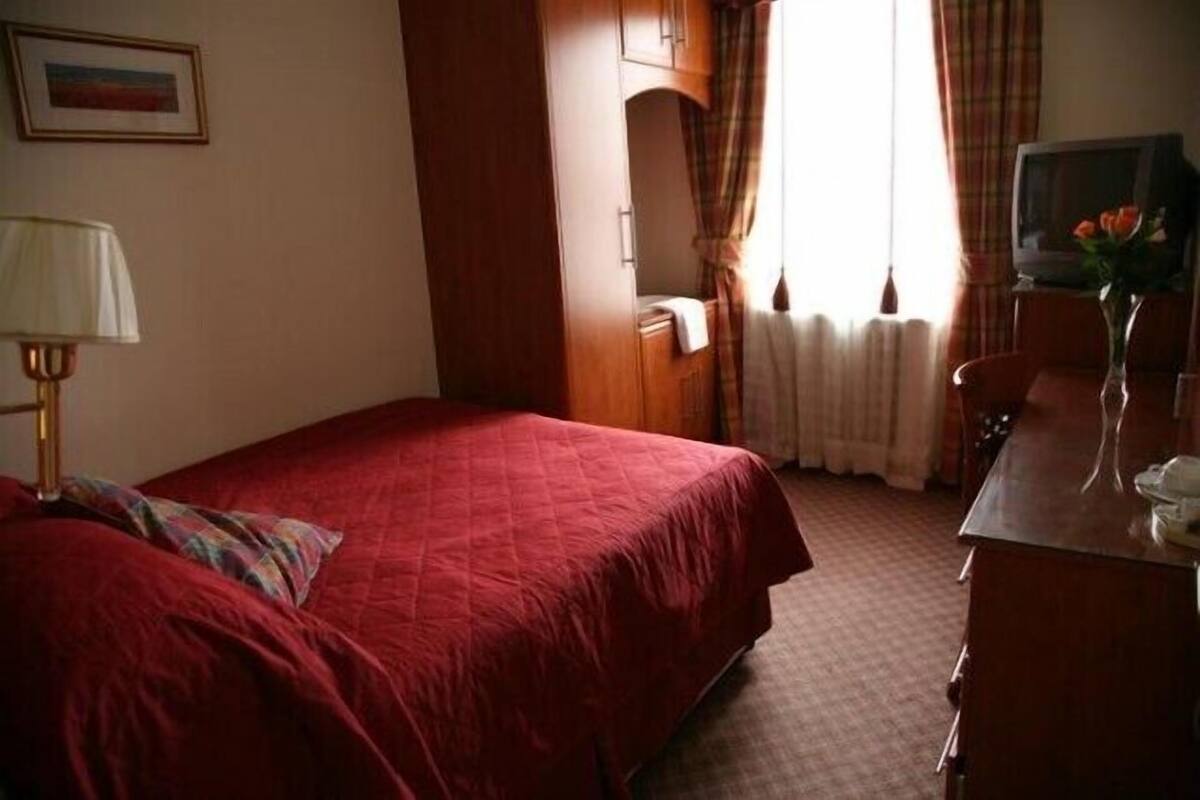 A hotel room with a bed, a desk, a chair, a TV, and a window with curtains.