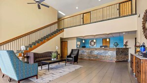 A spacious lobby with a staircase, a reception desk, and a seating area with a patterned armchair and a leather chair. - Best Western Liberty Inn (Delano)