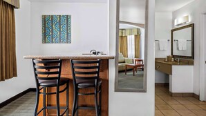 A hotel room with a kitchenette, two bar stools, a painting, a mirror, and a view into the living area. - Best Western Liberty Inn (Delano)