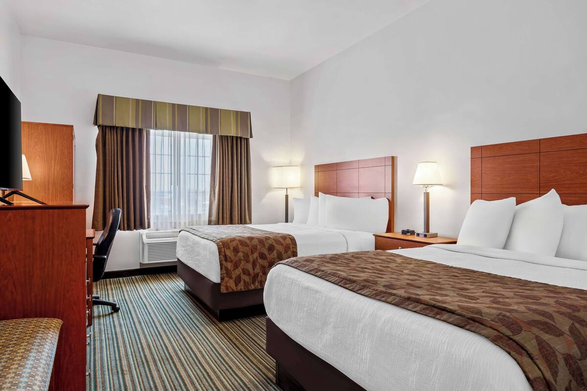 A hotel room with two beds, a desk, a chair, and a television.