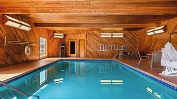 Una piscina interior con paredes y techo de madera, suelo de baldosas y una zona de estar con sillas y una mesa.