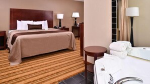 A hotel room with a large bed, a separate bathroom with a bathtub, and a small table. - Old Mill Inn (Omaha)