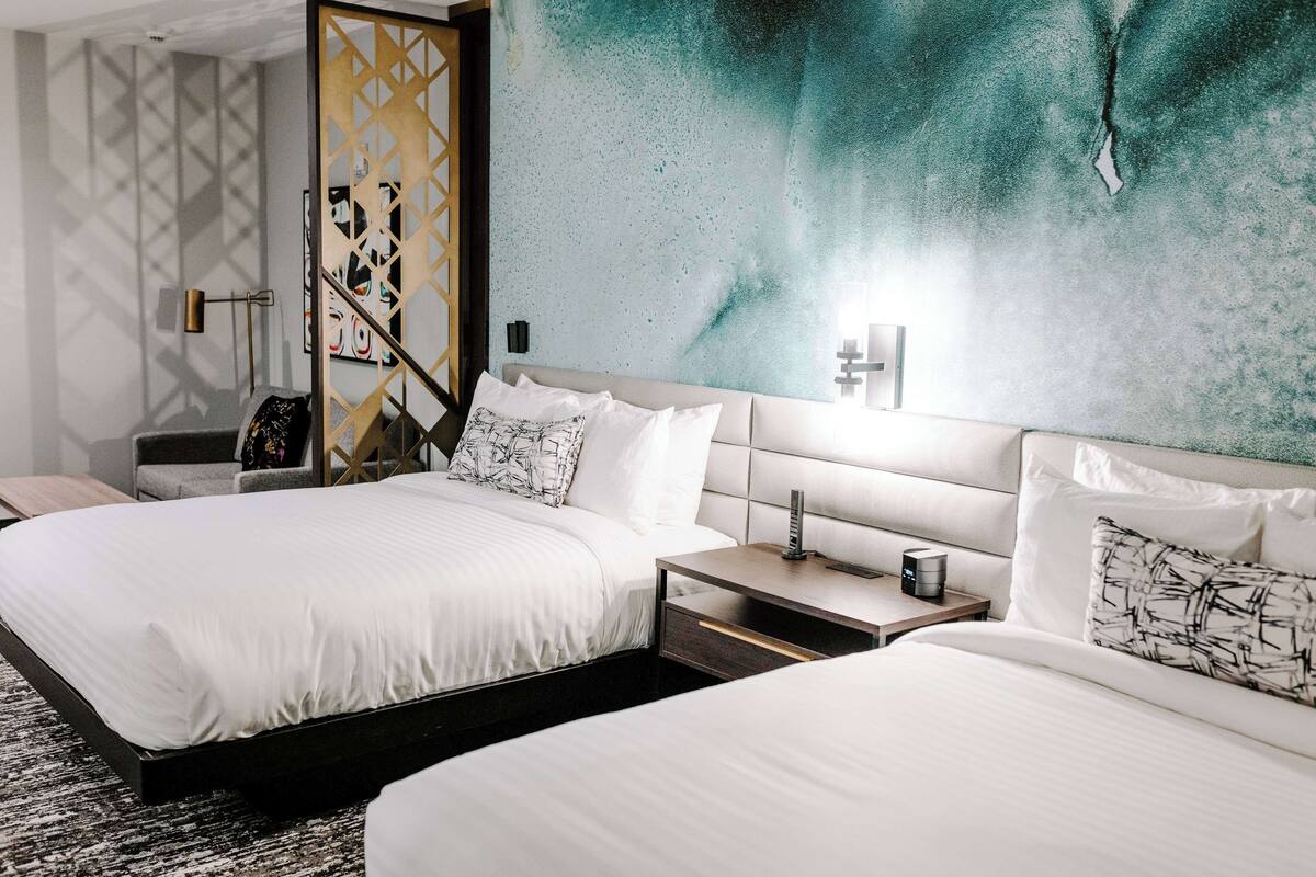 Une chambre d’hôtel avec deux lits, une table de chevet, une lampe et un mur au décor texturé.